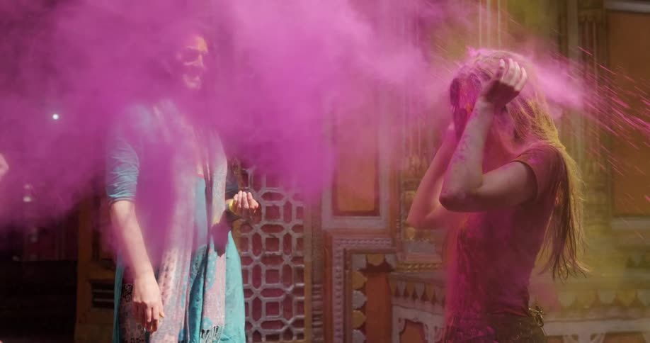 People throw colored powder onto young woman during holi as they stand near building