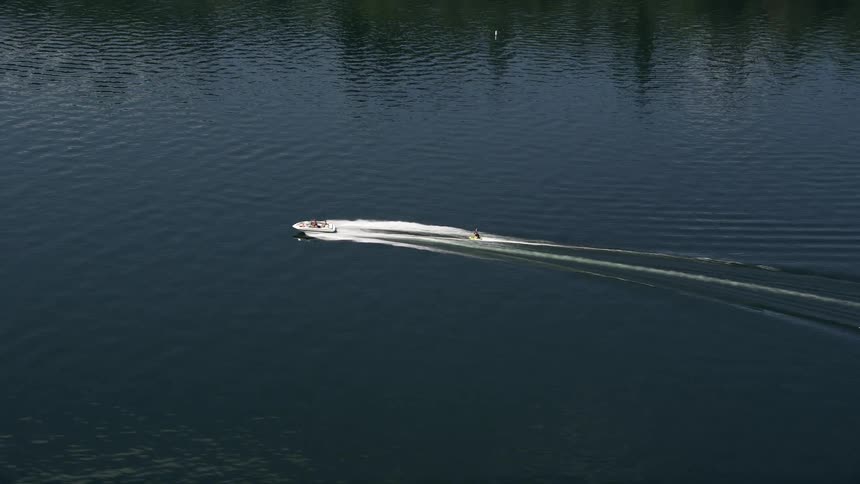 A speedboat pulls a raft on Lake Washington filmed from above surrounded by partly cloudy skies