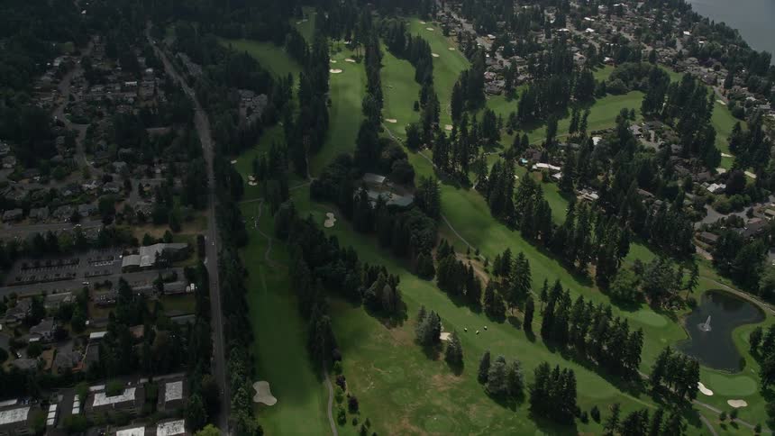 A birds eye view of Inglewood Golf Club by Lake Washington with partly cloudy skies showing the golf course surrounded by a residential neighborhood water and businesses in Kenmore Washington