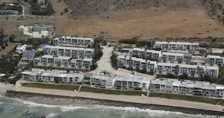 An aerial of houses built on the coastline as waves crash against the sand