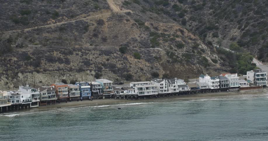 Drone view of houses along a beach coastline with a road behind the houses and a mountain behind the road