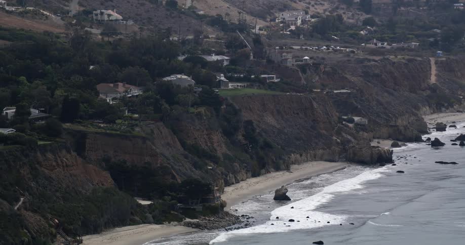 Waves crash onto the shore of a beach below a cliff