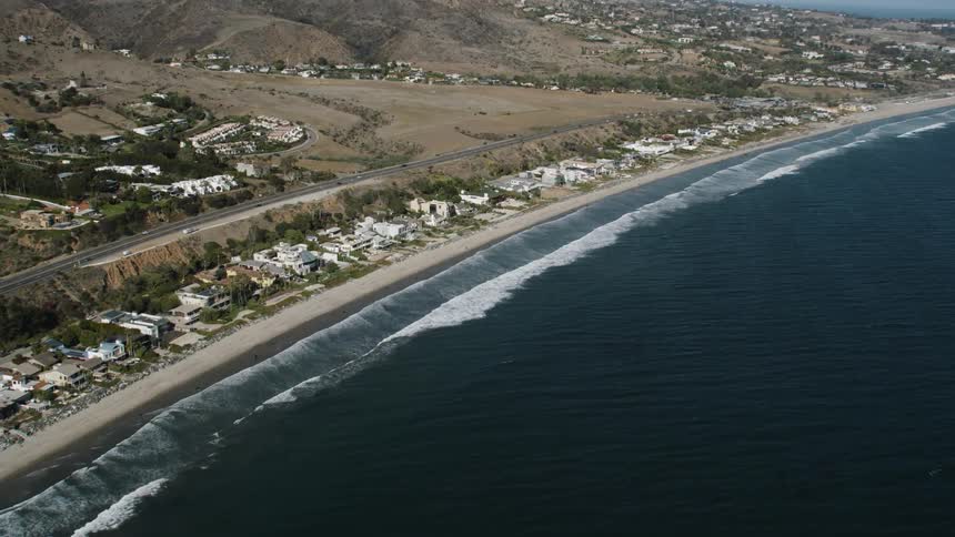 Waves crash onto the shore of a beach along a suburb