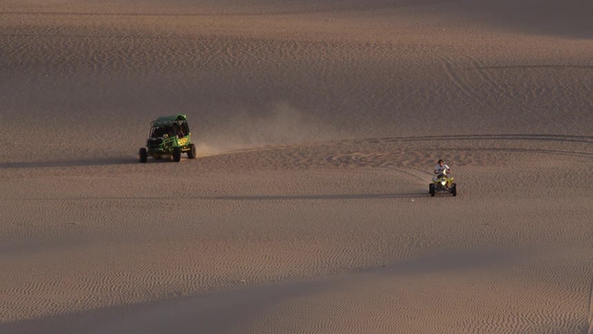 Two vehicles are traveling over desert sands
