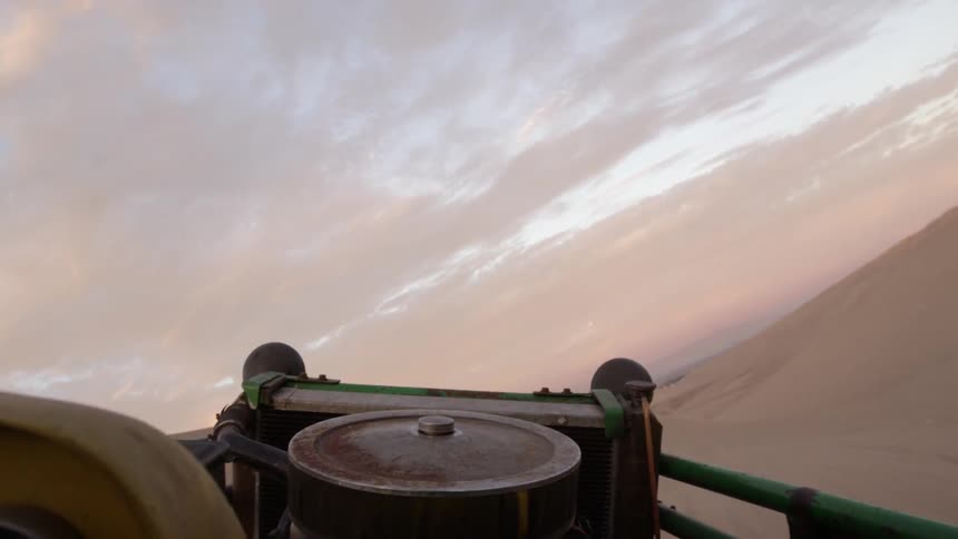 A vehicle is driving up a sand dune