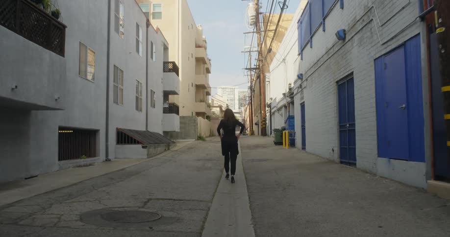 Woman walking down an alley between tall buildings on a sunny day in a metropolis