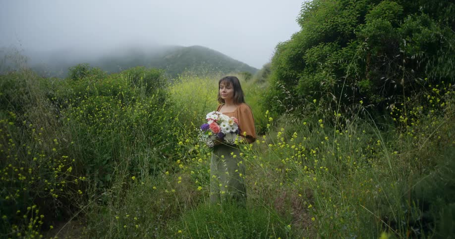 Woman with brown bangs blouse and green skirt holds a bunch of flowers in the field