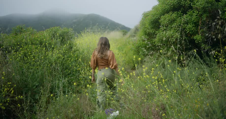 A woman drops wildflowers she picked in a field