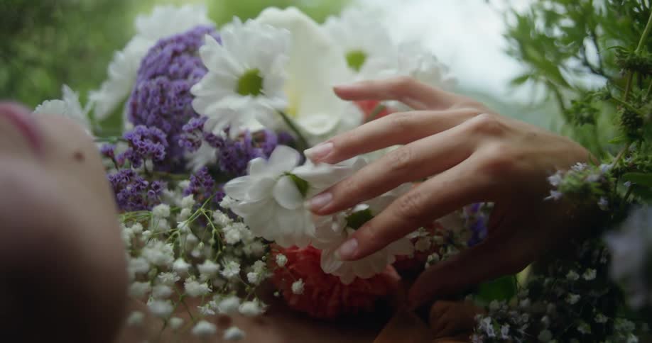 A woman is lying on the ground outside moving her hand over flowers covering her chest