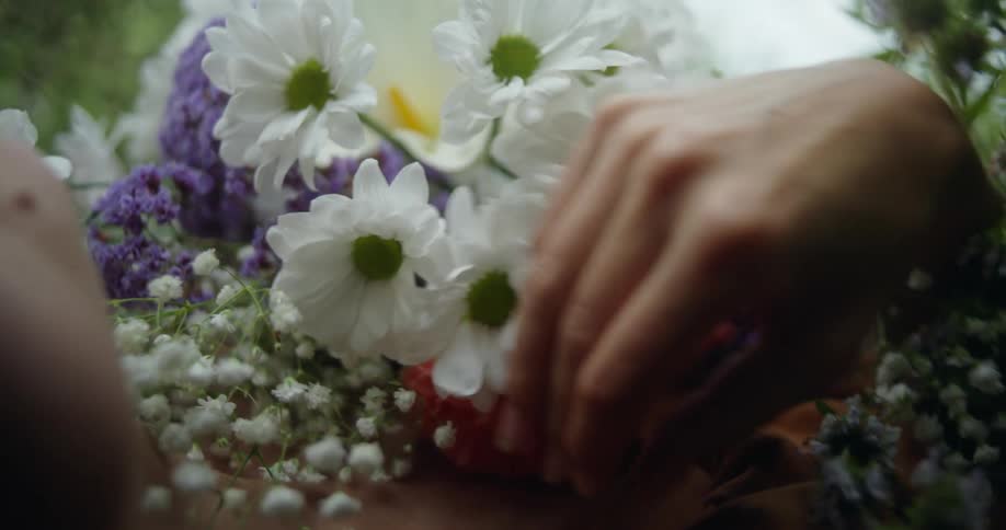 A woman is lying on the ground outside moving her hand over flowers covering her chest