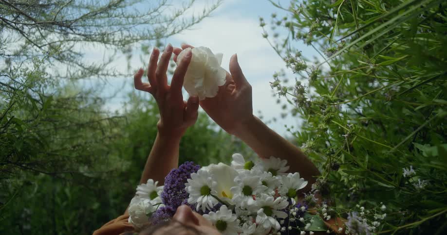 Close up of a woman covered in flowers on her chest as she lays on her back in the grass