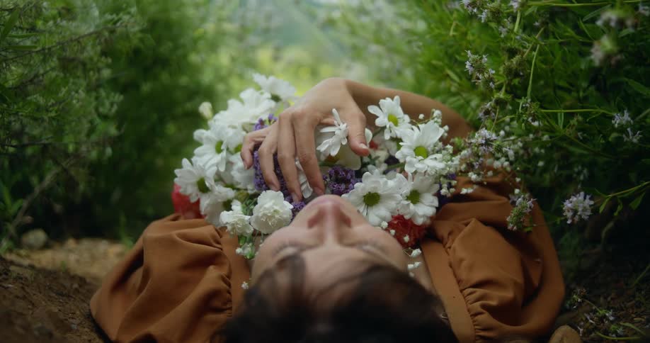 A young woman is laying down outdoors and holding bunch of flowers