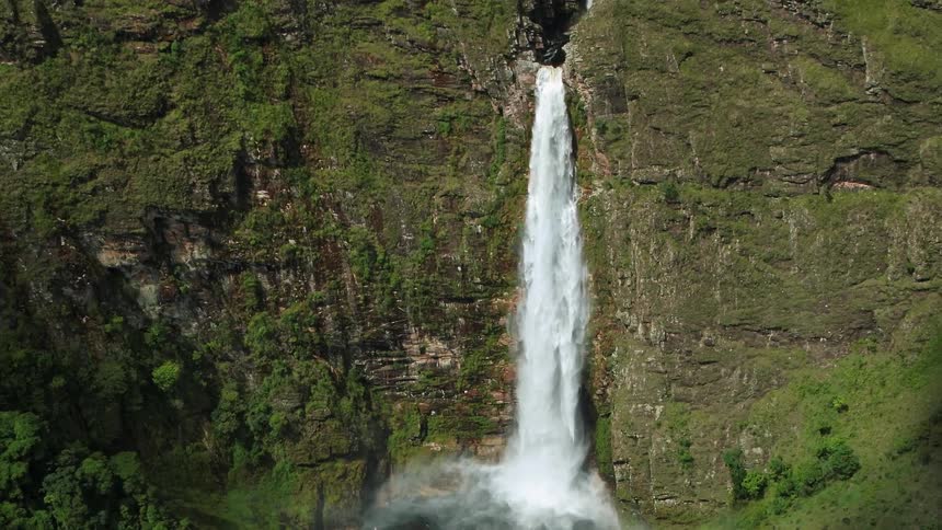 Waterfall emerges from cliff and falls to natural pool emptied by narrow stream