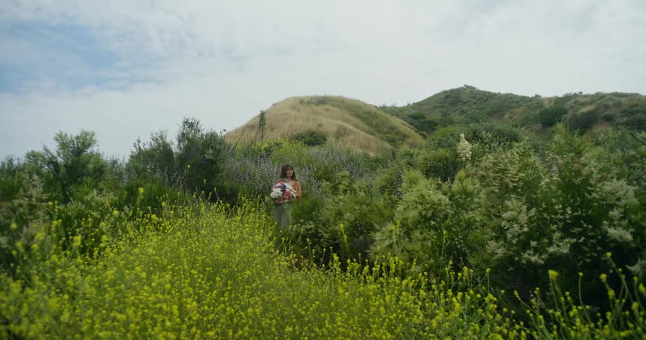 Theview is of a woman walking into a field of grass and flowers