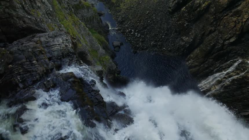 Waterfalls flow down cliffs to river in narrow valley