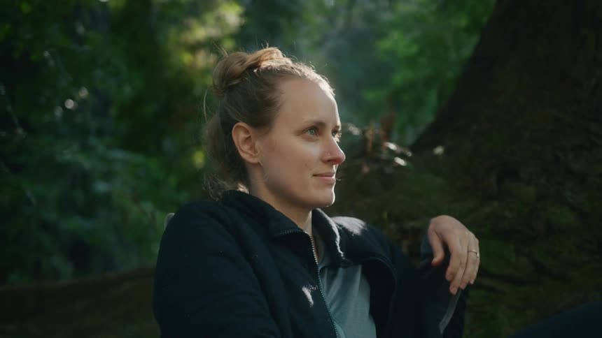 Young woman resting on the base of a large tree in the forest at morning