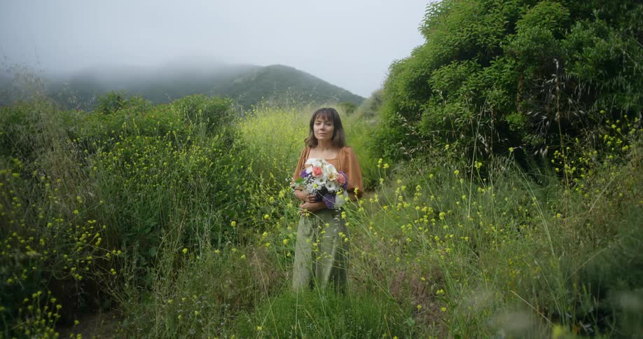 A woman is holding flowers while standing in the grass
