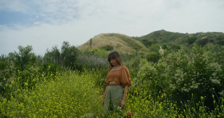 Young woman standing on a field at daytime throws down a bouquet of flowers
