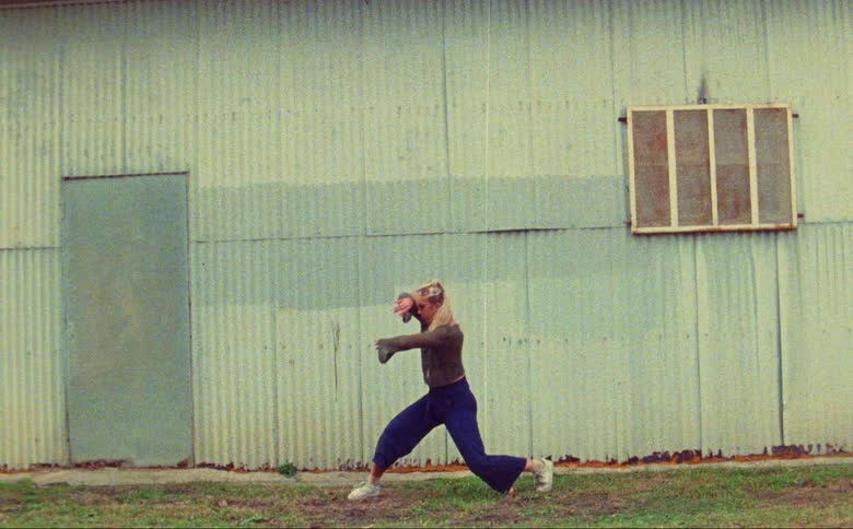 Young woman standing outside a rural building dance energetically caught on vintage film