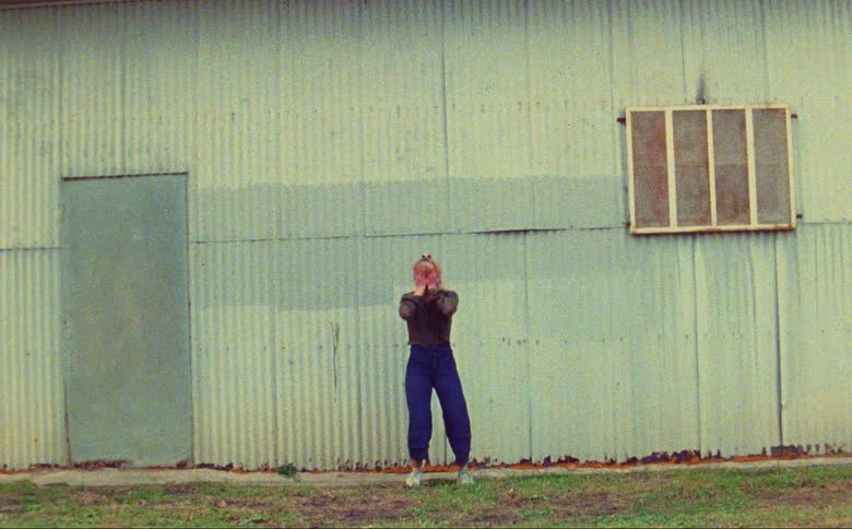 Female dancer dances outside corrugated panel building with a metal door