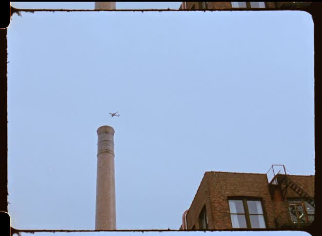 Airplane flying high in the sky over a building with a tall smoke stack