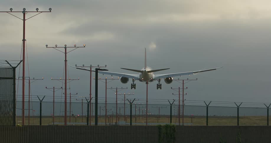 Airplane comes in for a landing as car drives past wall