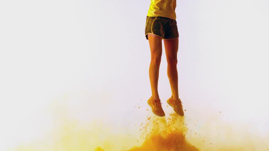A woman flying up into the air as yellow powder rises below her feet