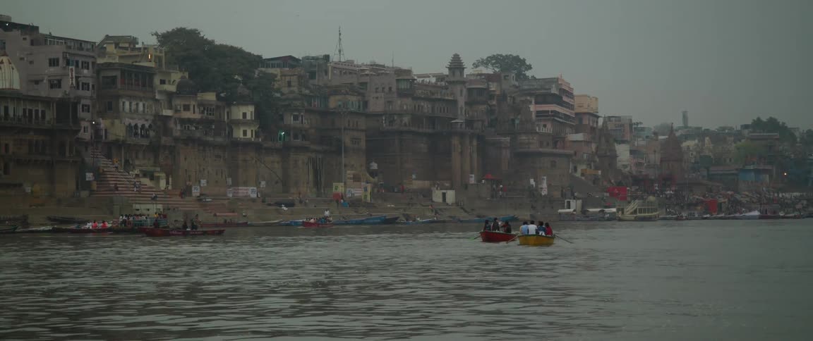 Two groups of people using small boats to travel across a body of water next to a third world city
