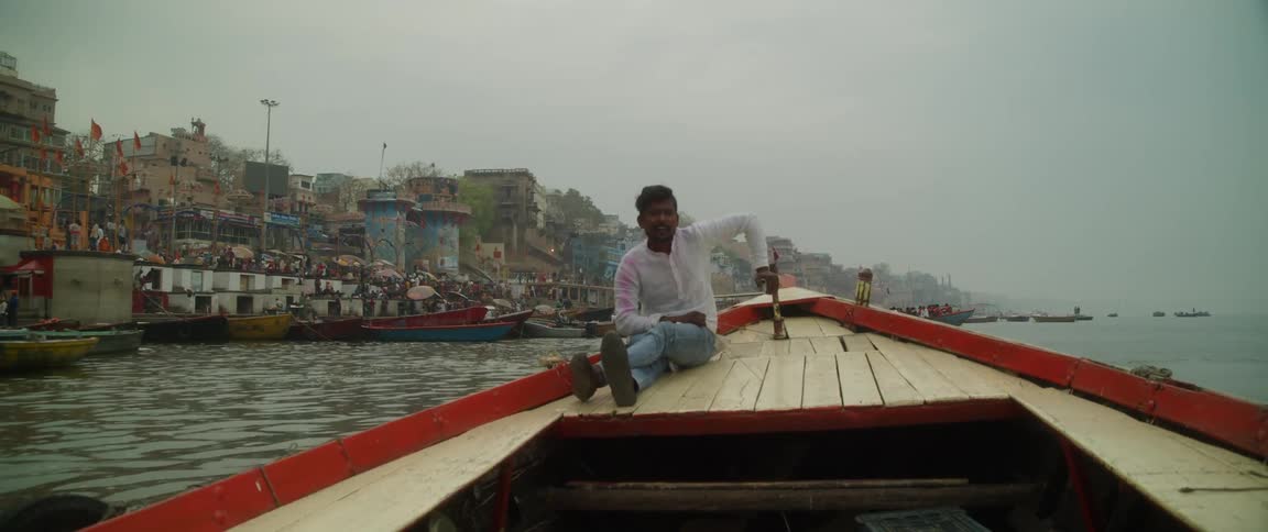 Man in shirt and jeans steers boat off the coast