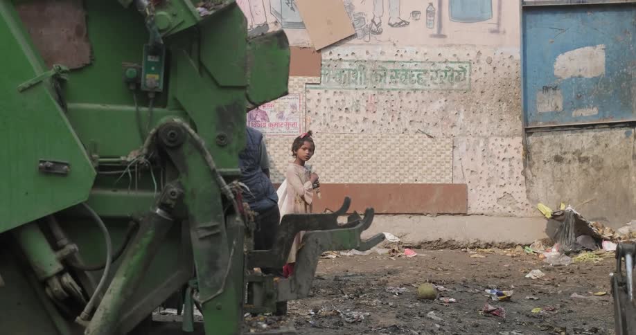 Young girl standing outdoors near a building in a third world country as she looks at people walking