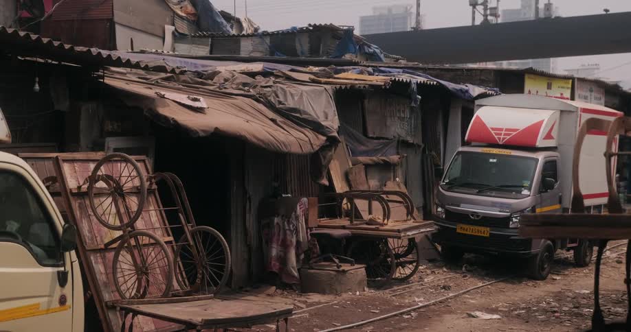 A truck is parked on an alley in front of a dilapidated building with scattered junk