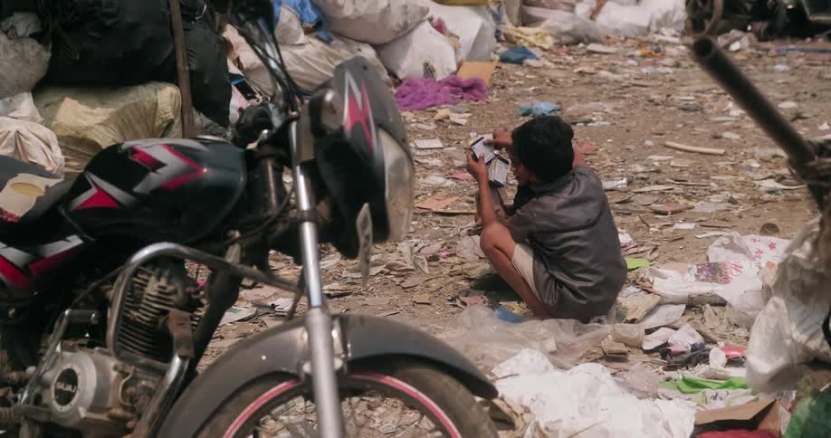 A young boy kneels in piles of trash in a slum