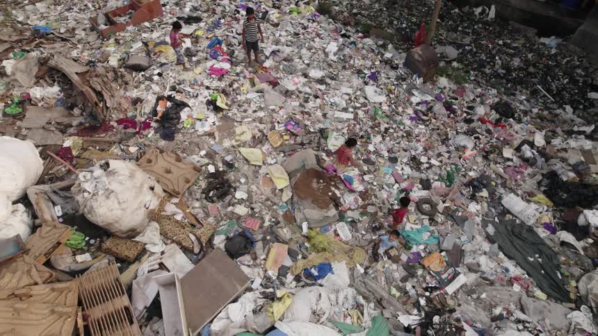 A group of children on a pile of garbage covering the streets of a slum plays catch with pieces of trash