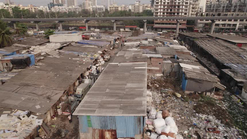 A slum with streets covered in garbage and shacks made of wood boards and metal plates is separated from a modern tower block only by a road and an overpass