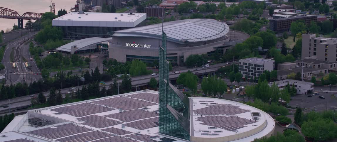 Highway passes stadium and building with multiple solar panelsnear river reflecting red of sun