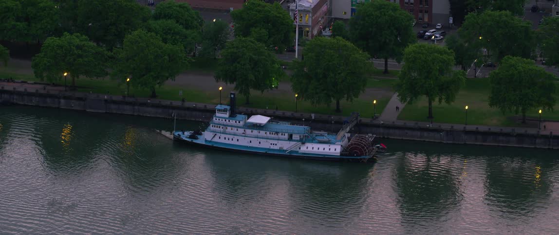 People move along riverfront passing docked riverboat