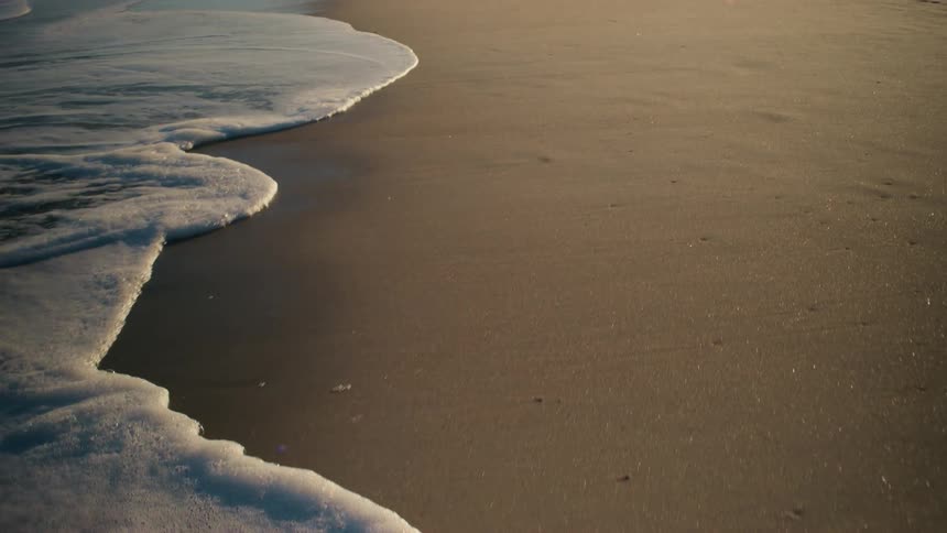 Ocean waves breaking against the sandy beach at sunset