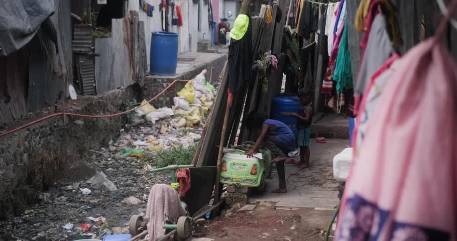 Two children a boy and a girl play in a dirty street with a toy car next to a broken wooden fence