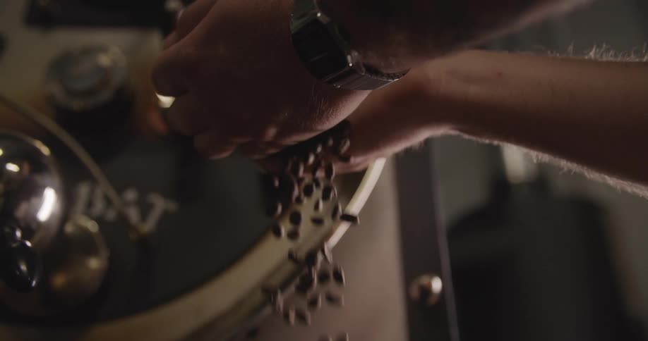 A man picks up and then slowly drops a handful of coffee beans