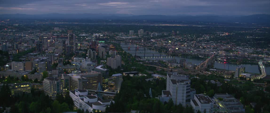 Multiple bridges span river crossing through city lit by lights after dusk