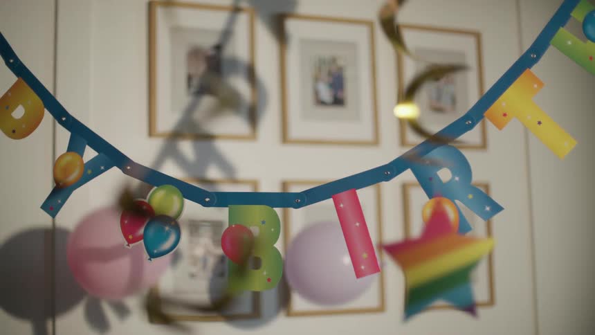 Three balloons fall to the floor behind a hanging sash saying happy birthday
