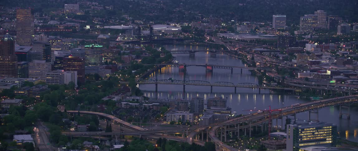 Traffic moves on roads and bridges across the river as building lights are on in the city