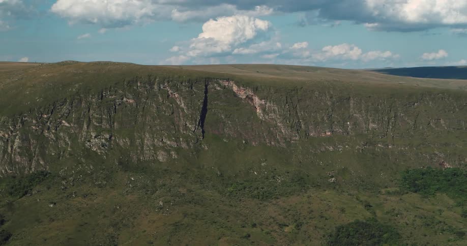 Trees nestle against base of cliff under a cloudy sky