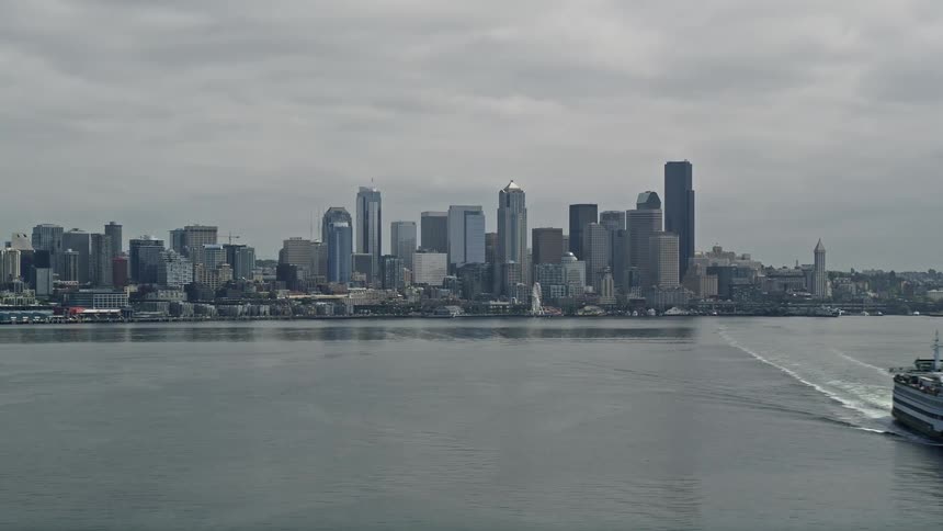 A ferry boat sails across Elliott Bay on a cloudy day revealing the iconic Space Needle and towering skyline of Downtown Seattle Washington