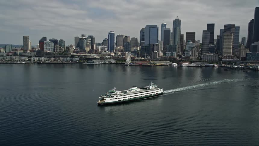 Aerial footage of a yacht sailing past downtown Seattle revealing the skyline and a ferry on Elliott Bay during a cloudy day