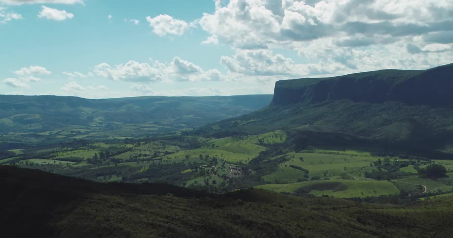 Valley of green hills stretches between cliffs and mountains