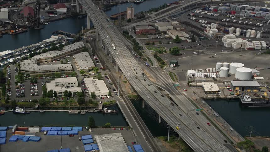 Approaching and tilting down from above this aerial footage captures the West Seattle Bridge and Harbor Island against a backdrop of cloudy skies and industrial docks offering a unique of the Seattle shipping industry