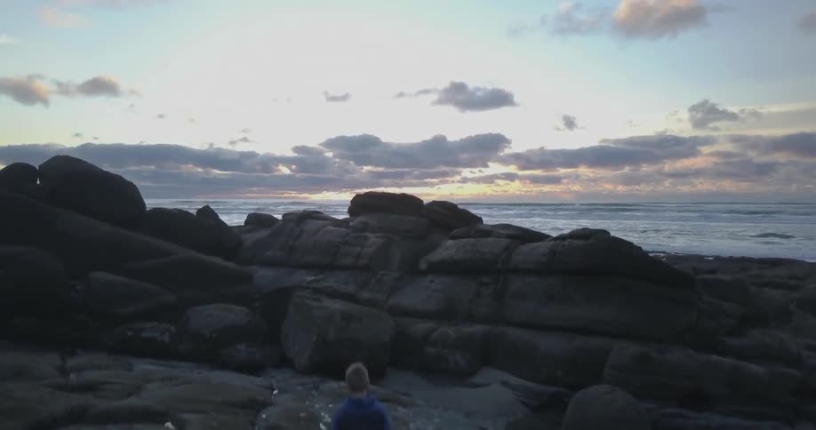 A boy climbs onto rocks on a beach