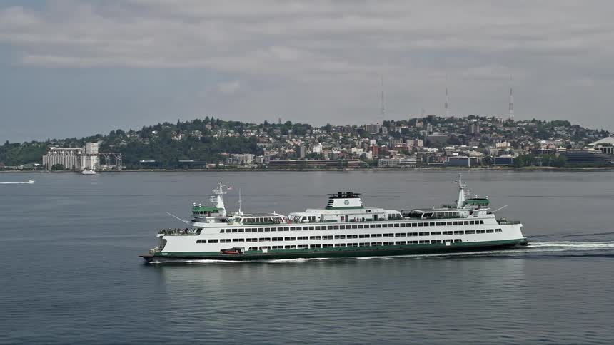 Aerial footage of a ferry sailing away from Seattles downtown area revealing the Space Needle and skyscrapers while passing through Elliott Bay in Washington