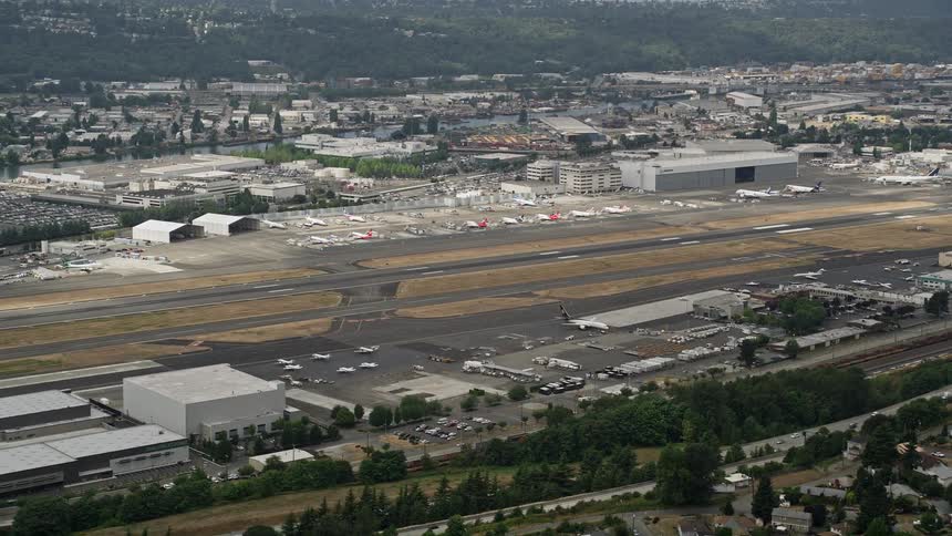 Aerial footage of commercial planes parked at Boeing Field in Seattle as traffic moves on a nearby street near houses and buildings in the mountainside